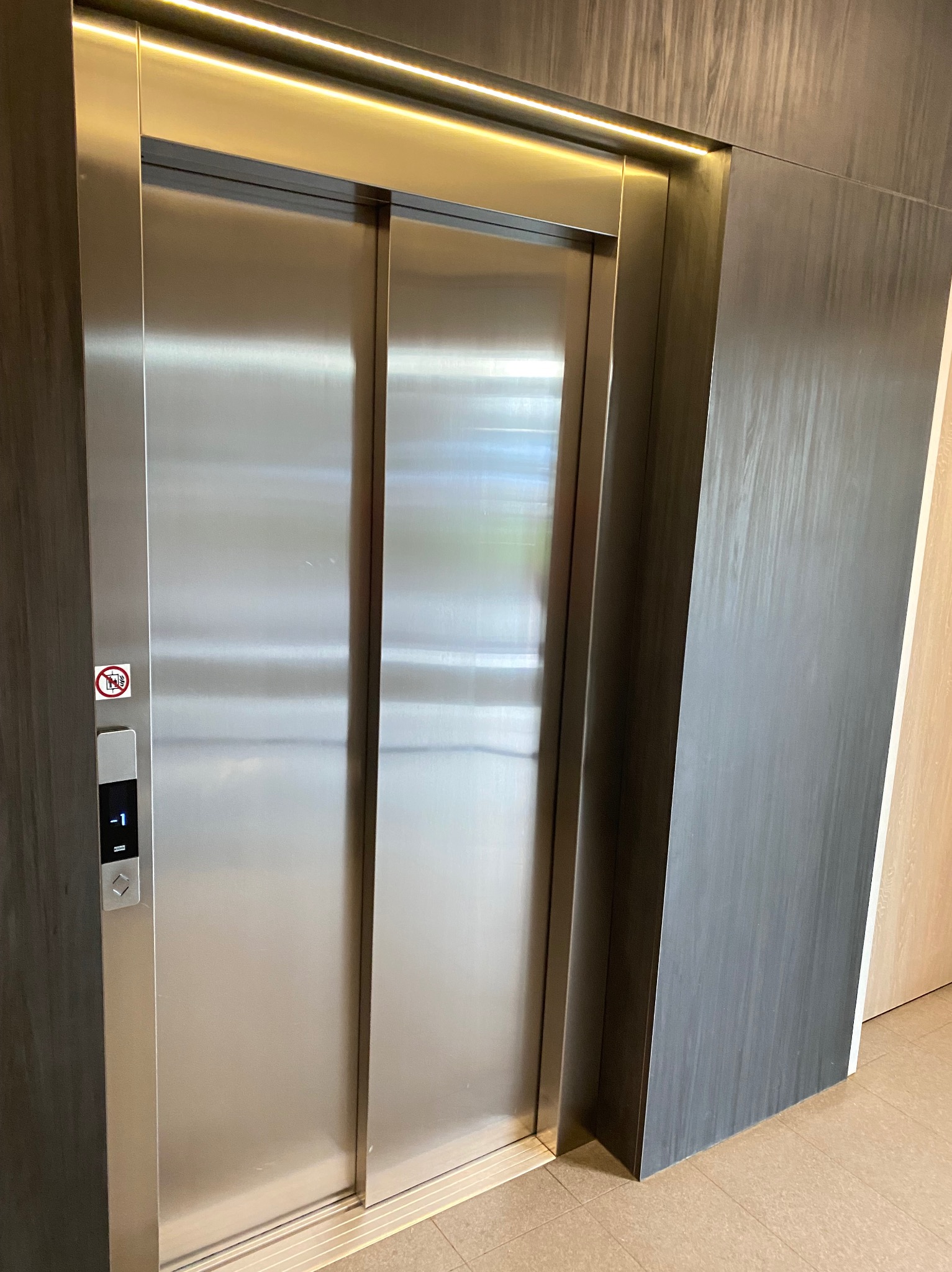 Błyszczące, metalowe drzwi windy osobowej z panelem sterowania na pierwszym planie, oświetlone górnym światłem LED.