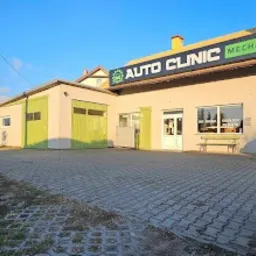 Budynek warsztatu Auto Clinic z zielonymi akcentami i napisem 'Mechanika Samochodowa' na fasadzie, widoczny z zewnątrz, w słoneczny dzień. Kostka brukowa na pierwszym planie.