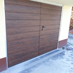 Firma Produkcyjno-Usługowo-Handlowa KamBlach Kamil Trzupek - Nowa, brązowa brama garażowa segmentowa z poziomym wzorem paneli, z zamkiem na klucz, zamontowana w jasnym budynku. Widoczny fragment kostki brukowej i szczotka.