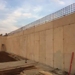 Wznoszenie betonowych ścian fundamentowych z widocznym zbrojeniem i szalunkiem, poziomica oparta o ścianę.