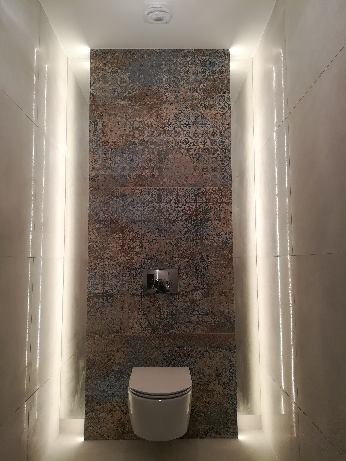 Nowoczesna toaleta z podświetleniem LED w wąskiej wnęce, ściana wyłożona dekoracyjnymi płytkami imitującymi stary wzór, bateria umywalkowa w kolorze chromu.