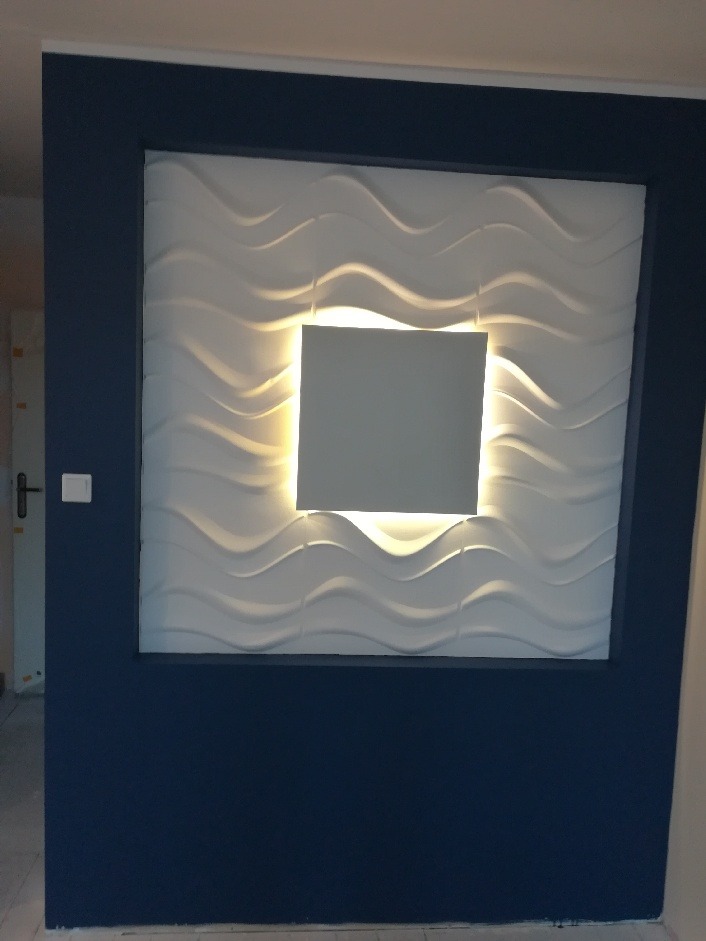 Niebieska ściana z białą, falistą płytą dekoracyjną podświetloną od tyłu, tworzącą efekt 3D.