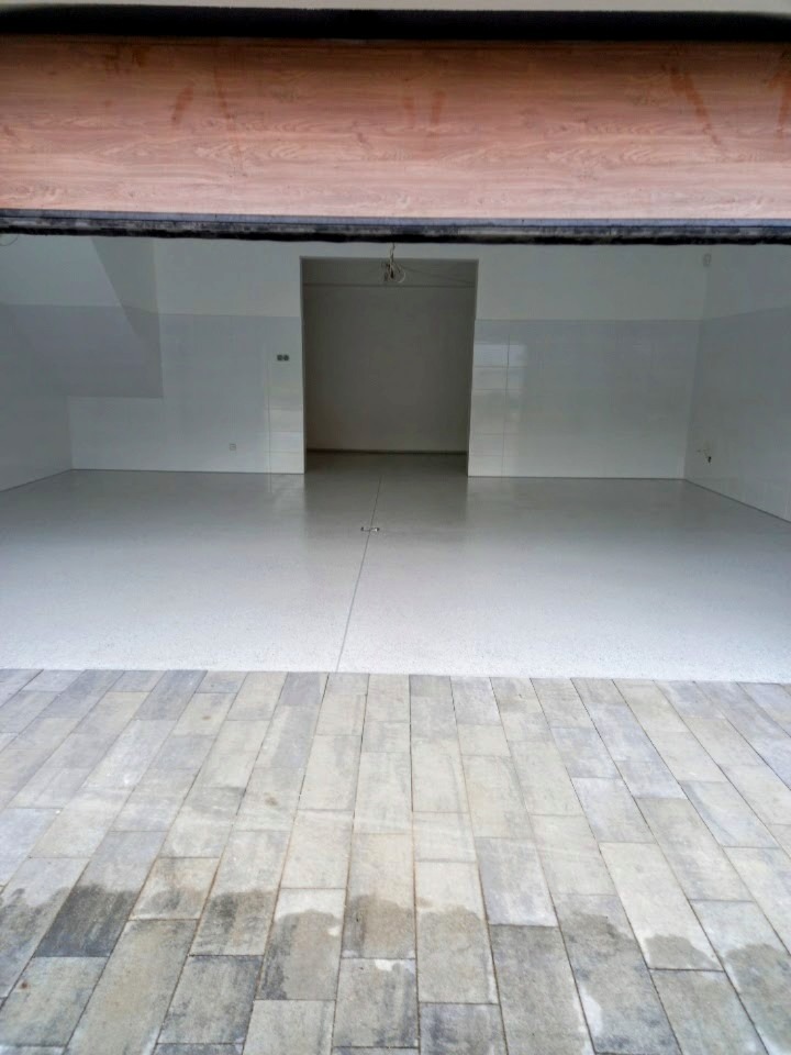 Jasnoszara, gładka posadzka w hali, widoczna z perspektywy kostki brukowej na zewnątrz. Świeżo wylana, jednolita powierzchnia.