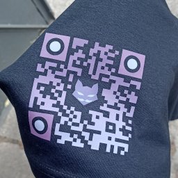 HAKAI Print - Ciemna koszulka z nadrukowanym fioletowo-białym kodem QR zawierającym w centrum stylizowaną głowę kota, trzymana w dłoni na tle chodnika.