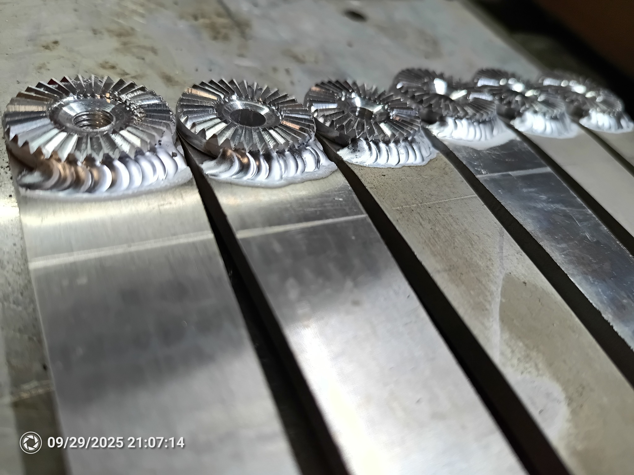 Precyzyjne spawanie: Szereg identycznych, metalowych elementów z ząbkowaną krawędzią, trwale połączonych ze stalowymi płaskownikami. Widoczne ślady spawania.