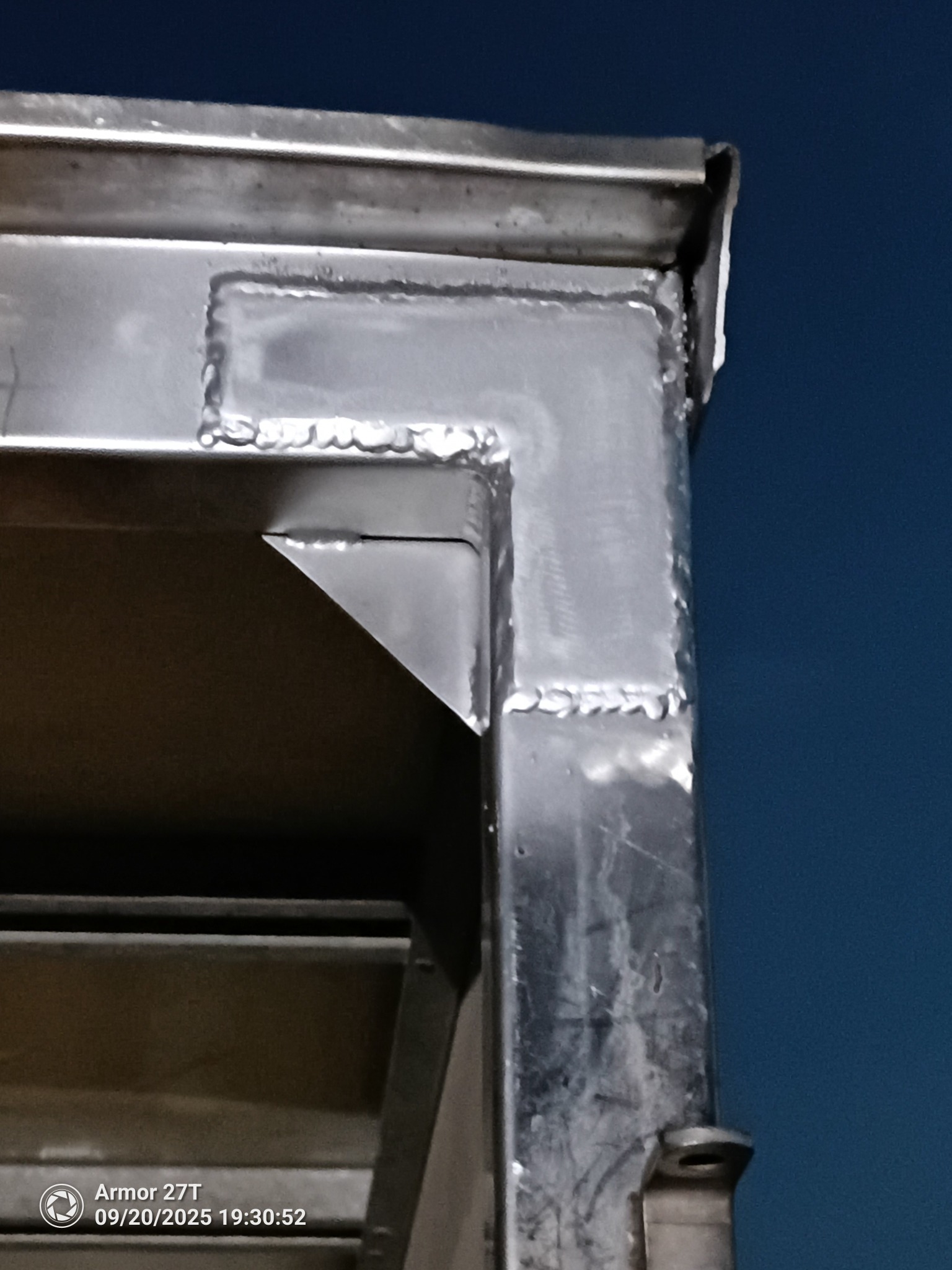 Precyzyjne spawy narożne konstrukcji metalowej w Kiezmarku. Widoczne ślady po obróbce, surowy metal, ciemne tło. Detal wykonania.