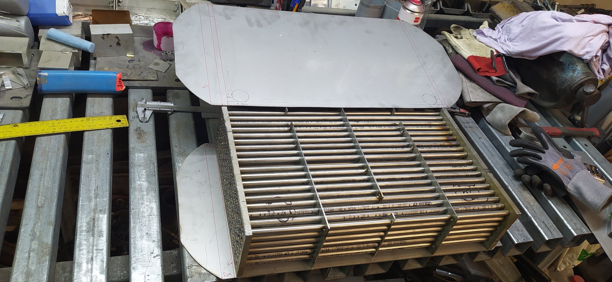 Wymiennik ciepła z rurkami ze stali nierdzewnej w trakcie produkcji. Widoczne elementy konstrukcyjne, narzędzia pomiarowe i odzież robocza w tle.