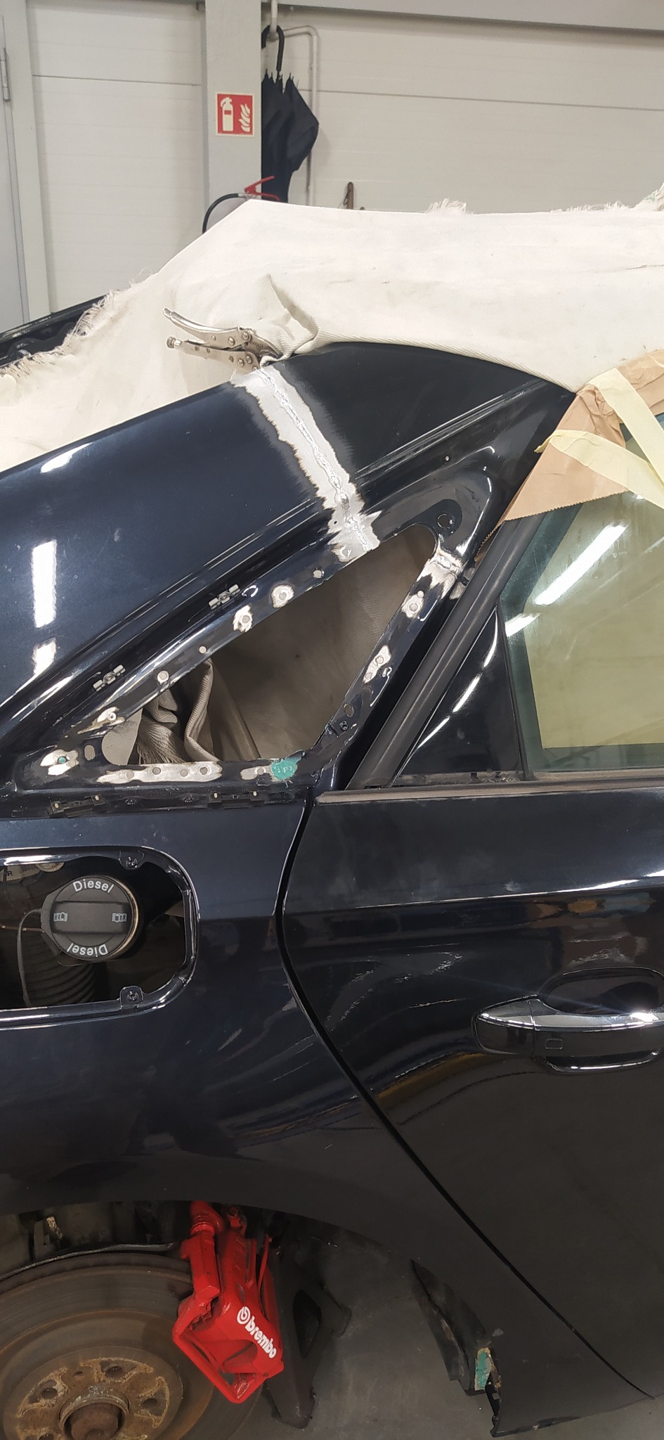 Fragment karoserii auta w trakcie naprawy blacharskiej. Widoczne ślady spawania i szlifowania, zabezpieczone elementy. Prace naprawcze w warsztacie.