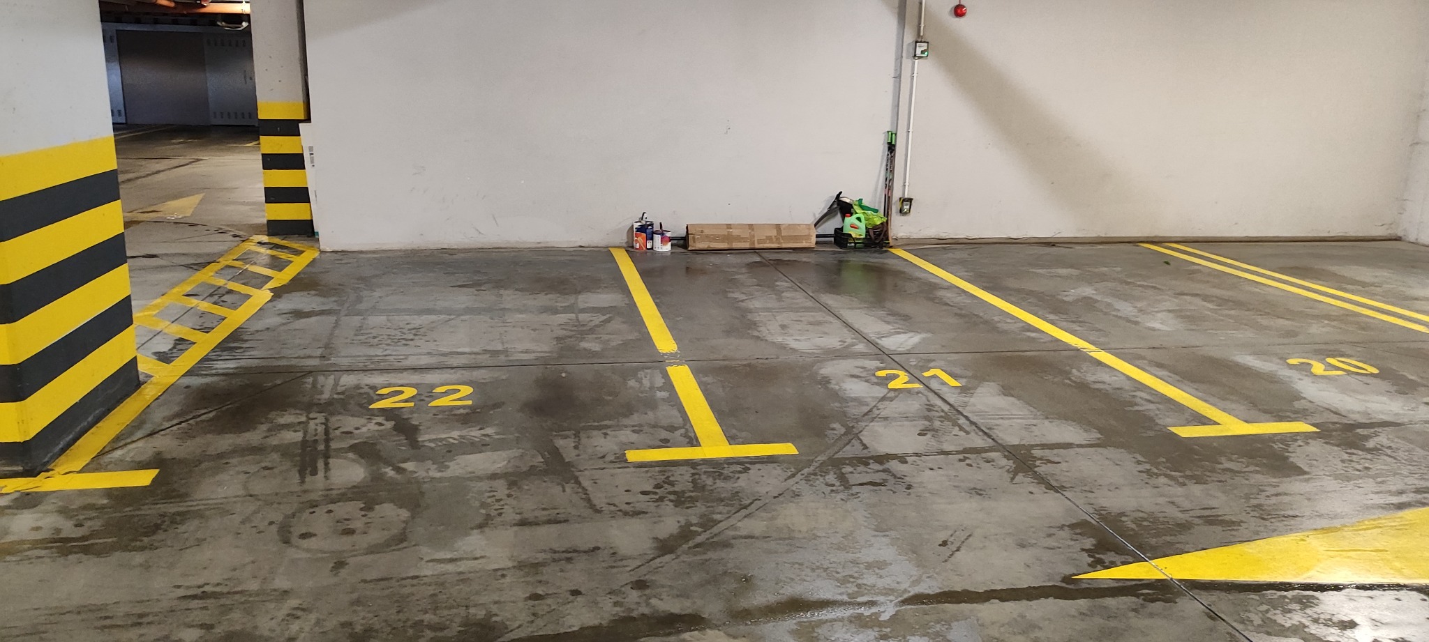 Oznakowane, żółtą farbą, miejsca parkingowe w garażu podziemnym. Widoczne numery 20, 21 i 22. Na ścianie puszki z farbą i narzędzia malarskie.