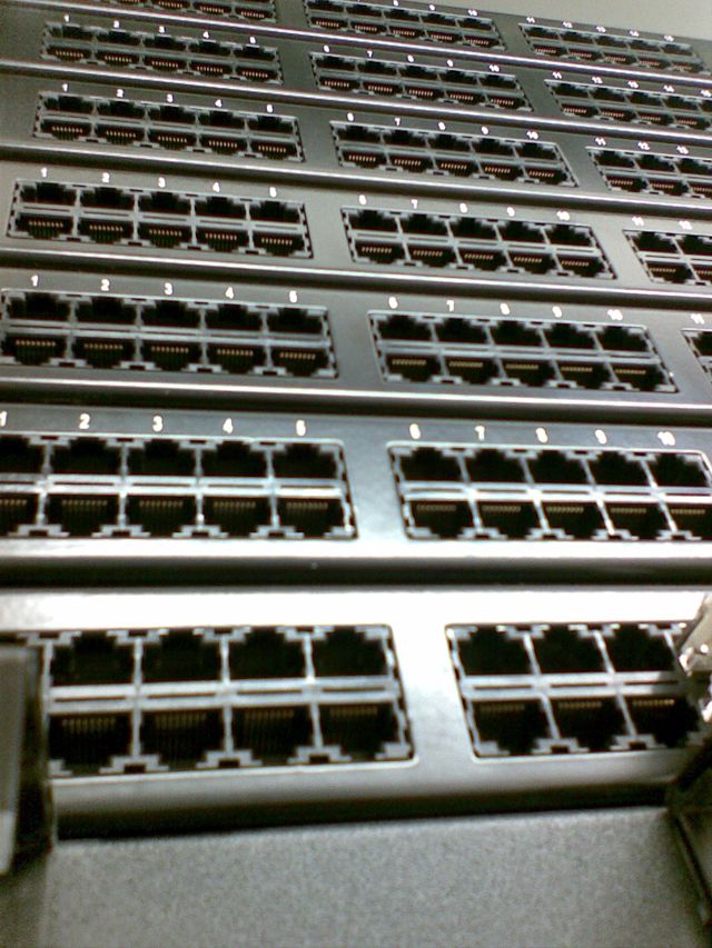 Panel krosowniczy z portami RJ45, widok z bliska pod kątem, numery portów nad gniazdami.