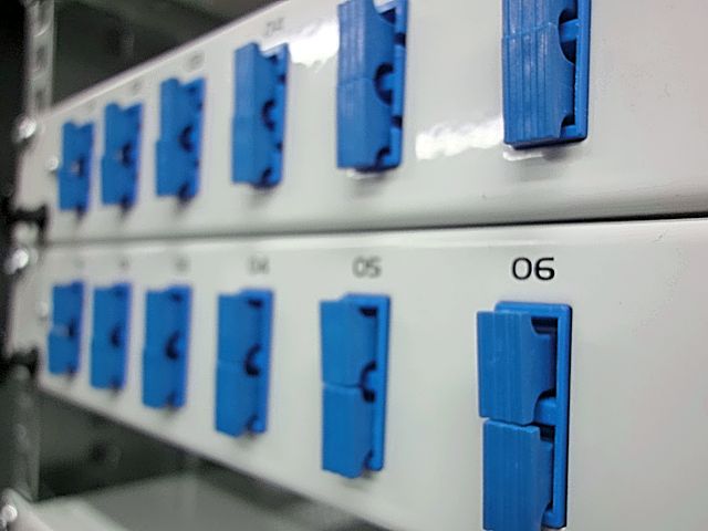 Panel krosowniczy światłowodowy z niebieskimi złączami, widoczne porty oznaczone numerami 01-06, ujęcie z boku.