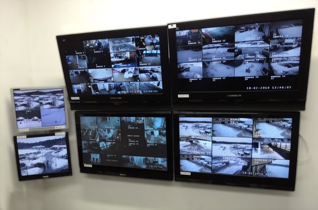 Ściana z kilkoma monitorami wyświetlającymi obraz z kamer monitoringu w różnych lokalizacjach, w tym wnętrza i tereny zewnętrzne pokryte śniegiem.
