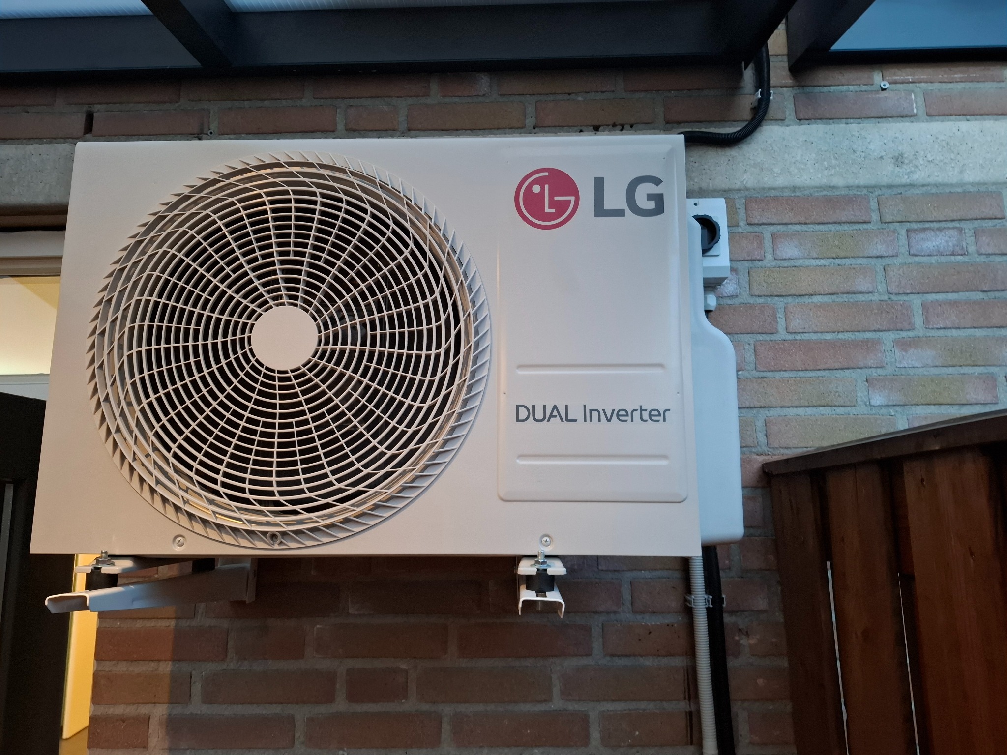 Zamontowana jednostka zewnętrzna klimatyzacji LG Dual Inverter na ceglanej ścianie, widoczne elementy instalacji i mocowania. Ujęcie z bliska.