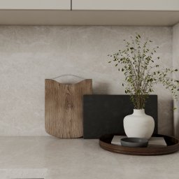 invero studio - Beżowa kuchnia z marmurowym blatem, drewnianą deską, czarną płytą i wazonem z zielonymi gałązkami na tacy. Minimalistyczny design, neutralna kolorystyka, elegancki detal.