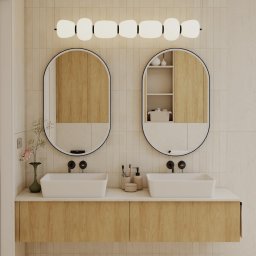 invero studio - Nowoczesna łazienka z dwoma umywalkami nablatowymi, drewnianą szafką pod umywalką i podłużnym oświetleniem nad lustrami w kształcie owalu z czarną ramą.