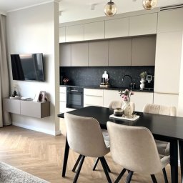 invero studio - Nowoczesna kuchnia z jadalnią: beżowe szafki, czarny blat, stół z krzesłami. Parkiet w jodełkę, wiszące lampy. Minimalistyczny design, jasne wnętrze.