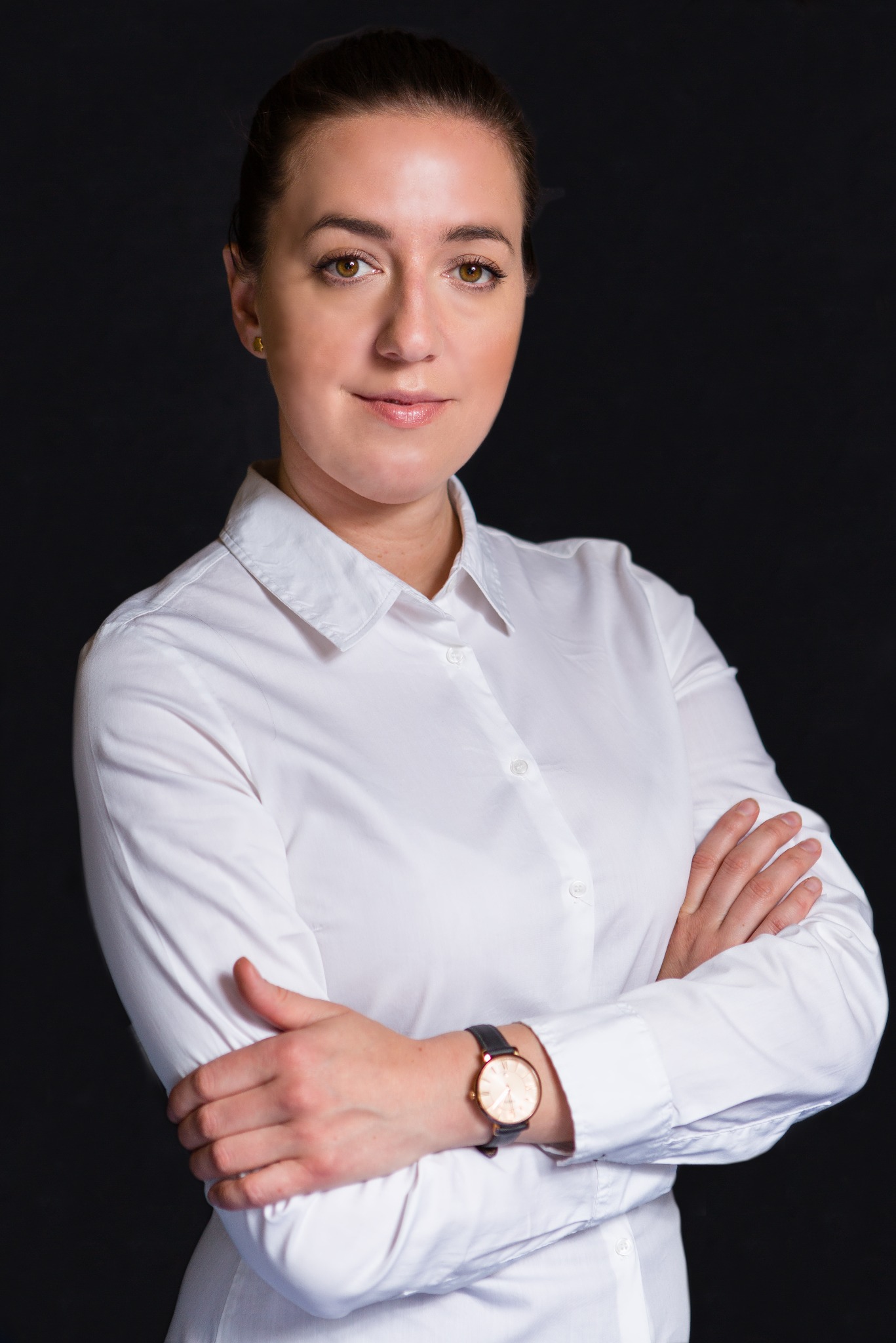 Portret kobiety w białej koszuli z założonymi rękami, na czarnym tle, z zegarkiem na nadgarstku.