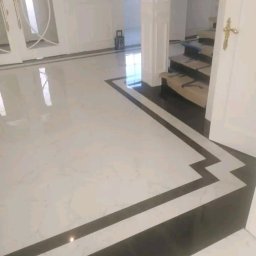 Jacek Sadowski - Błyszcząca podłoga z białych i czarnych płytek, zdobiona wzorem w zygzaki, prowadząca do białych drzwi i schodów w eleganckim wnętrzu.