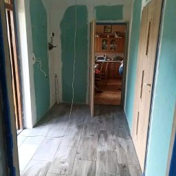 Jacek Sadowski - Korytarz w trakcie prac wykończeniowych: położona podłoga z płytek imitujących drewno, ściany przygotowane do malowania, widoczne instalacje elektryczne.