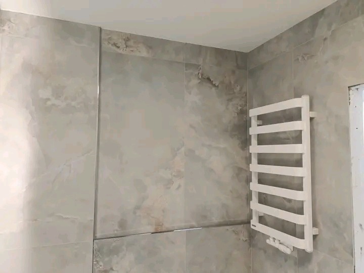 Wykończona łazienka z grzejnikiem drabinkowym i szarymi płytkami imitującymi marmur. Widoczne fugi. Minimalistyczny design.