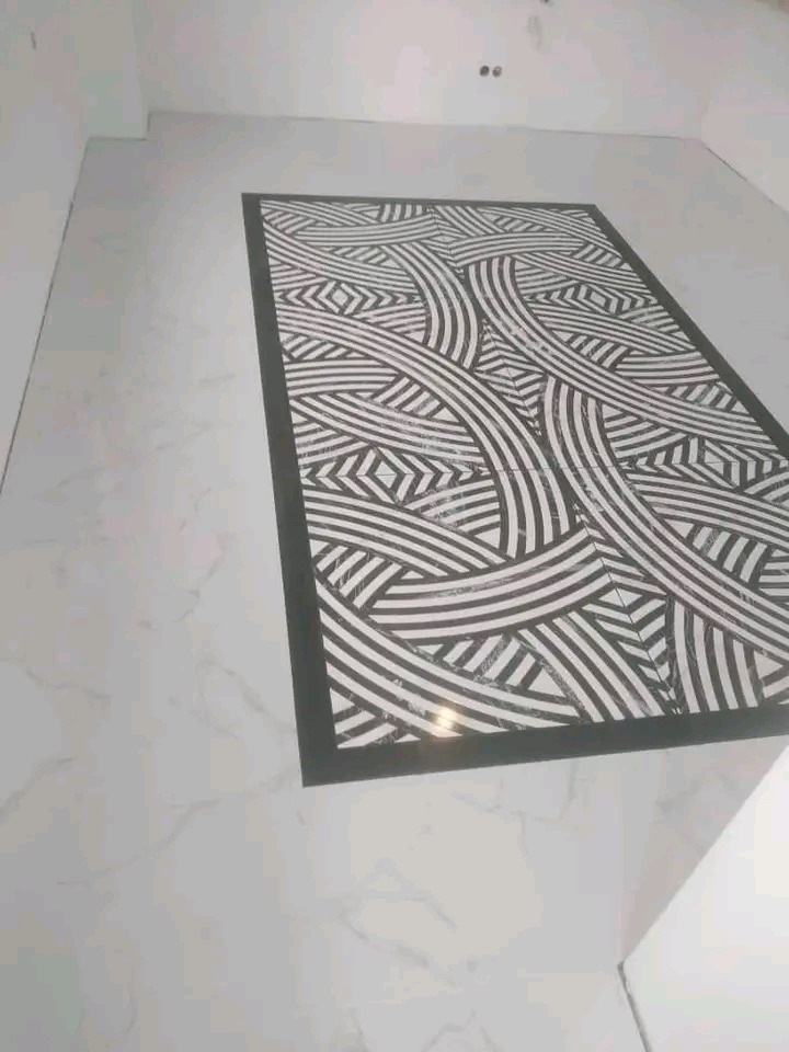 Ułożona podłoga z białych płytek z marmurkowym wzorem i czarnym, prostokątnym dywanem z geometrycznym deseniem na środku. Widok z góry.