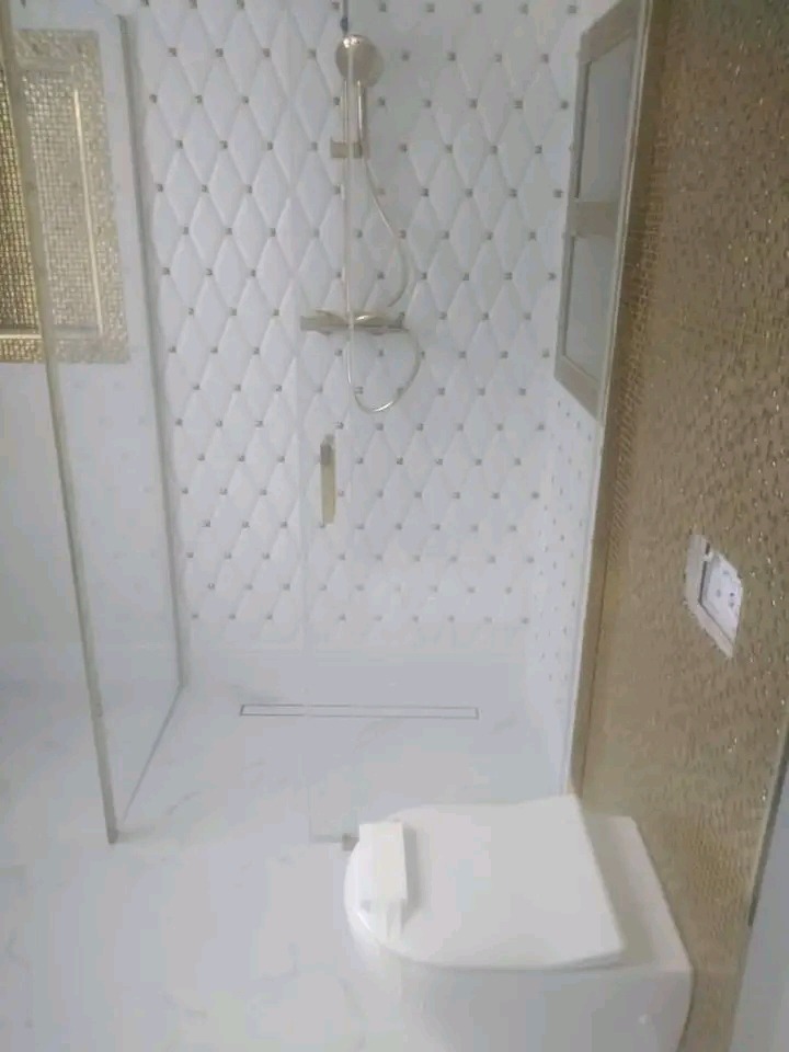 Elegancka łazienka z kabiną prysznicową typu walk-in, białą armaturą i dekoracyjnymi płytkami ściennymi w romby z subtelnymi, złotymi akcentami.