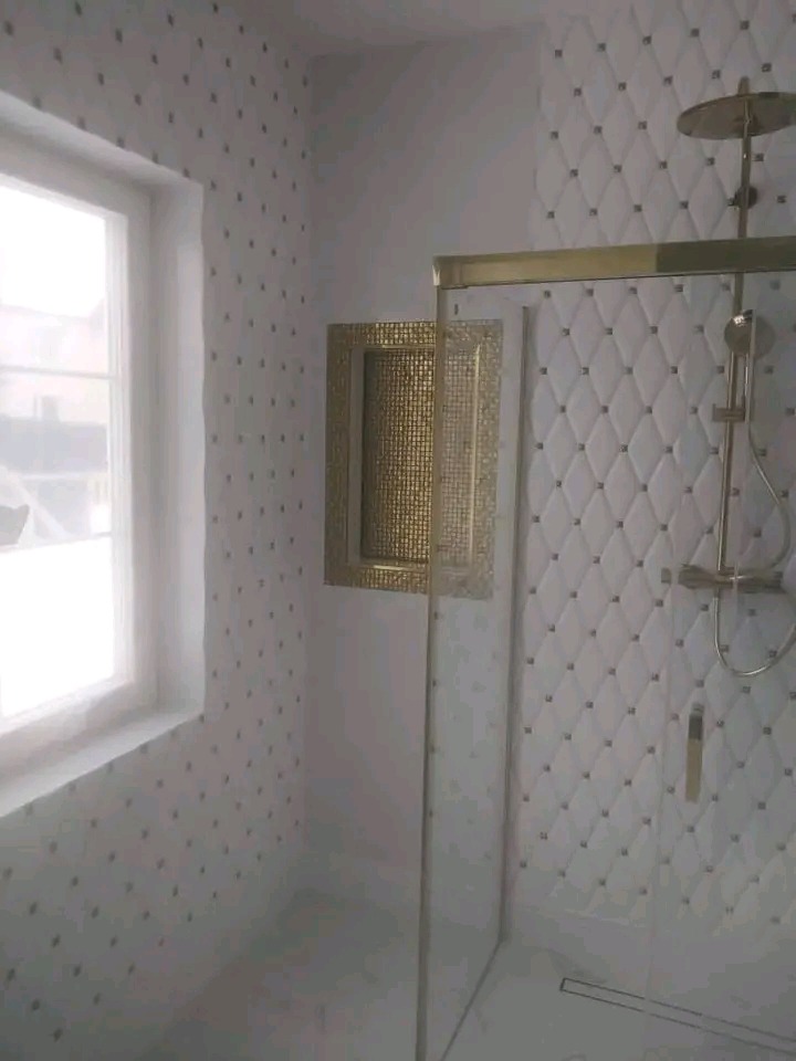 Wykończona łazienka z kabiną prysznicową, złotymi akcentami i ozdobną wnęką. Ściany wyłożone płytkami w romby i delikatne wzory.