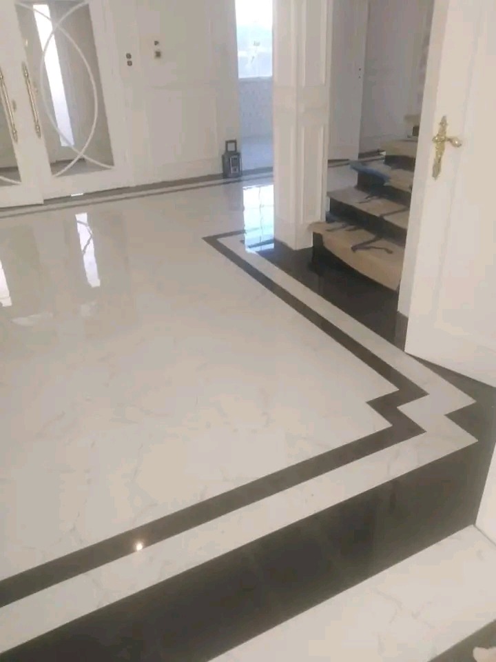 Błyszcząca podłoga z białych i czarnych płytek, zdobiona wzorem w zygzaki, prowadząca do białych drzwi i schodów w eleganckim wnętrzu.