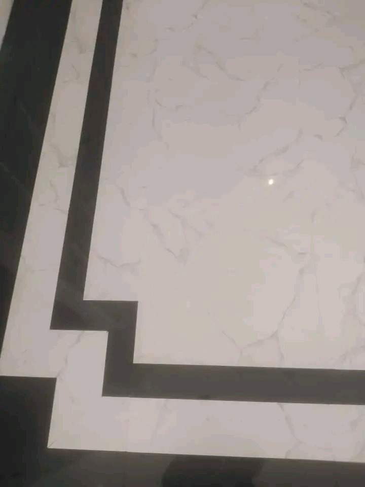 Wykończona podłoga z białych płytek imitujących marmur, z czarnym, geometrycznym wzorem wzdłuż krawędzi. Widok z góry, z bliska.