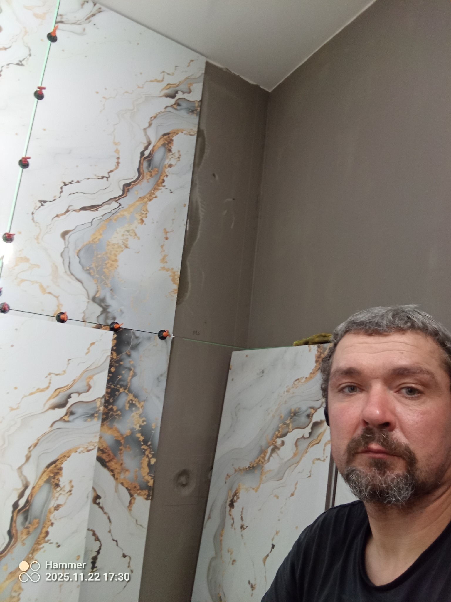 Układanie płytek imitujących marmur w Malborku. Widoczne systemy poziomowania płytek. Częściowo wykończona ściana i osoba w kadrze.