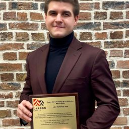 PROSPECT R.E.INVEST SPÓŁKA Z OGRANICZONĄ ODPOWIEDZIALNOŚCIĄ - Agent nieruchomości Marcin Biały z nagrodą 'Lider Sprzedaży 2024' na tle ceglanej ściany. Profesjonalny wizerunek biura Carbon Estate.