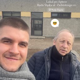 PROSPECT R.E.INVEST SPÓŁKA Z OGRANICZONĄ ODPOWIEDZIALNOŚCIĄ - Selfie dwóch mężczyzn na tle budynku z napisem 'Sprzedane i przekazane. Lokal po Aptece. Ruda Śląska'.