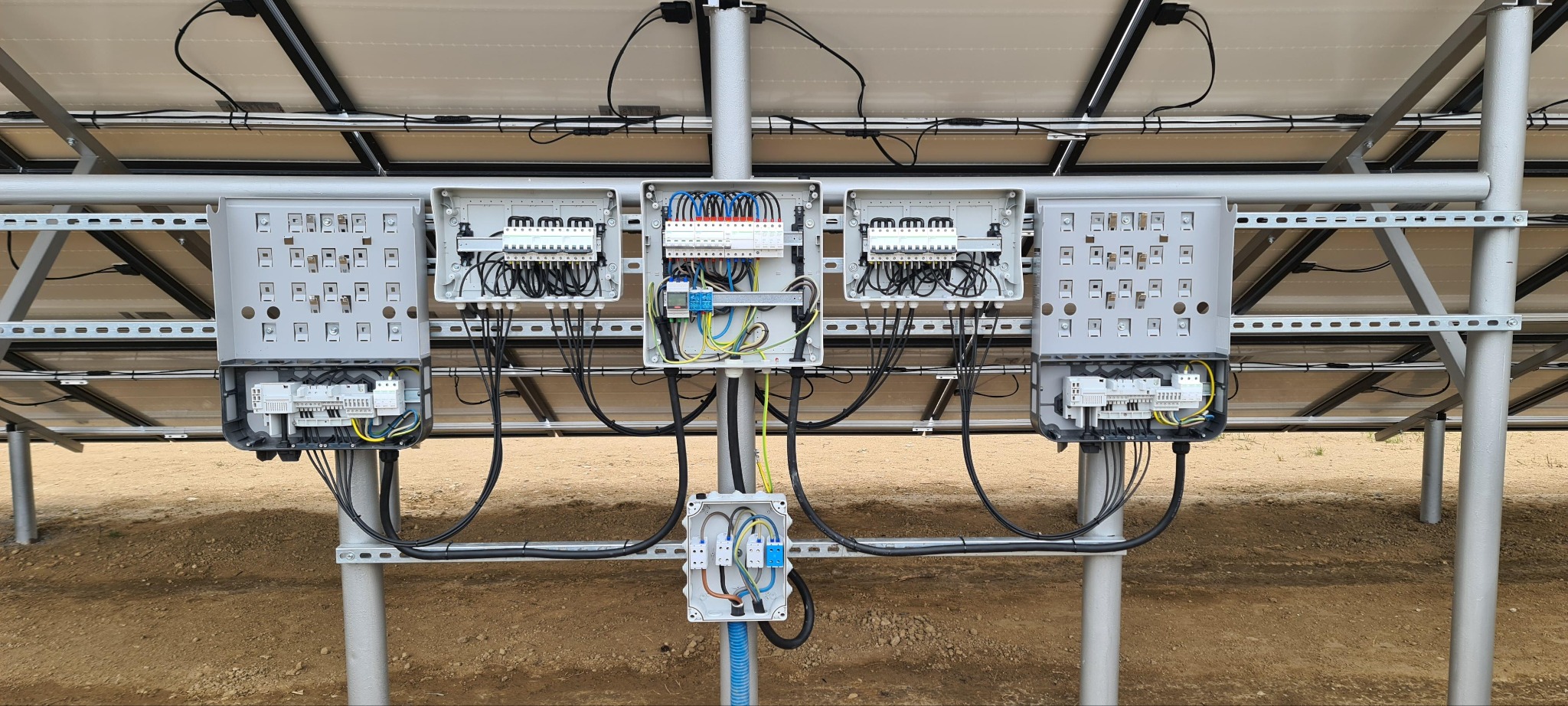 Rozdzielnice elektryczne pod panelami słonecznymi, widok od spodu. Skrzynki z okablowaniem zamontowane na metalowej konstrukcji wsporczej.