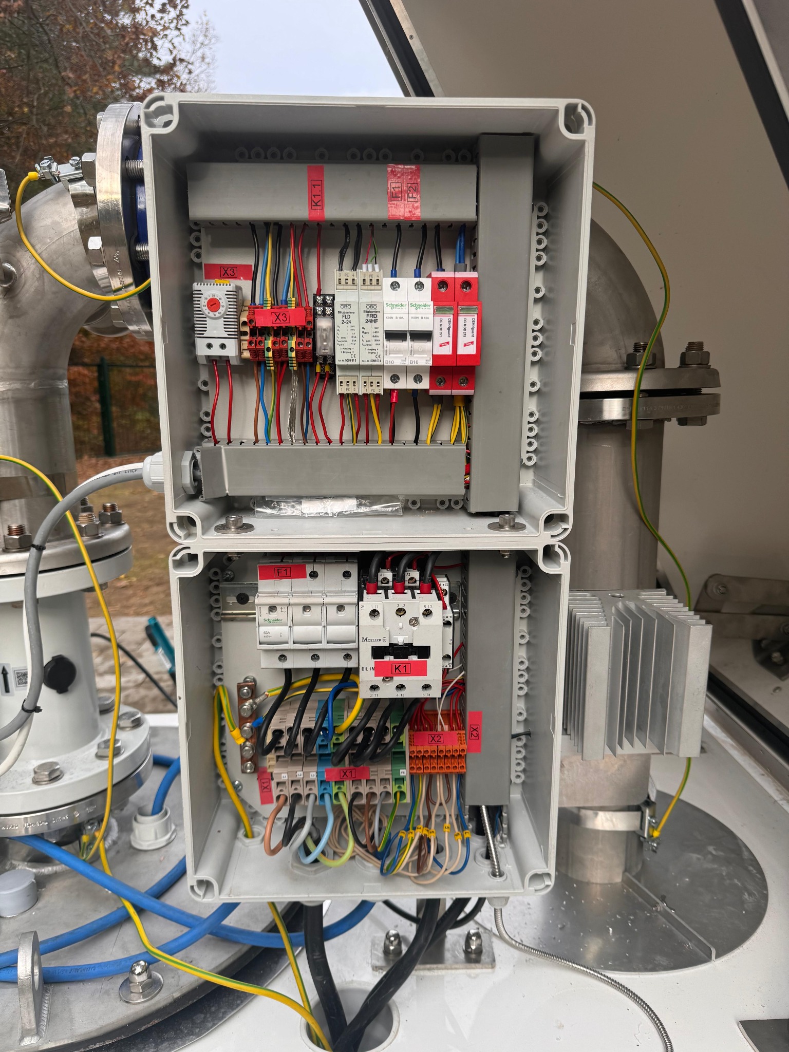 Otwarta, dwuczęściowa skrzynka elektryczna z widocznymi przewodami, bezpiecznikami i elementami instalacji odgromowej, zamontowana na metalowej konstrukcji rurowej.