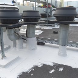 HydroRoof Hydroizolacje Dachów Płaskich Płynnymi Membranami Patryk Przekwas - Wykończony dach płaski z trzema kominami wentylacyjnymi, zabezpieczonymi białą powłoką hydroizolacyjną. Widoczne elementy instalacji i konstrukcji wsporcze.