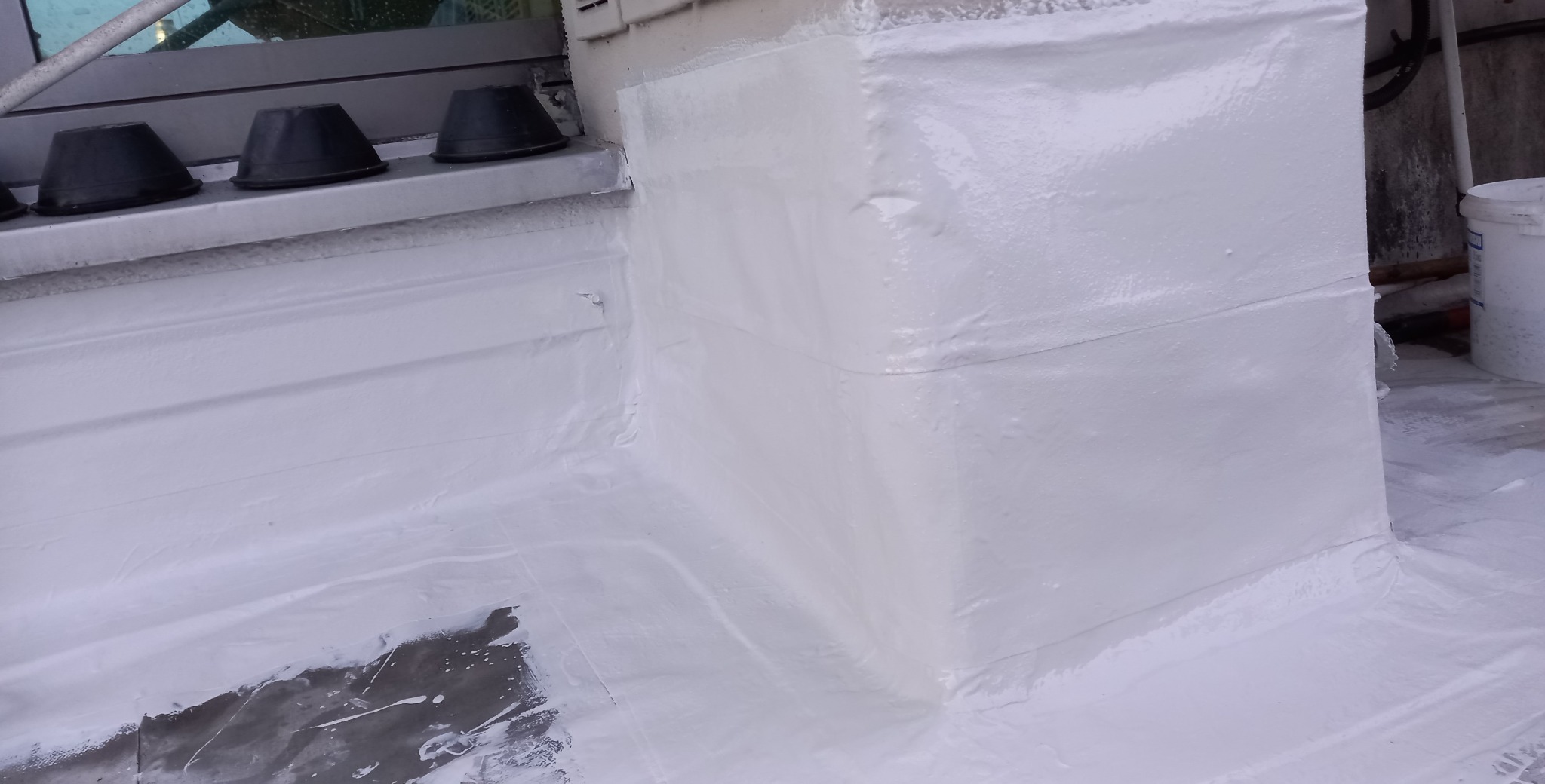 Biała hydroizolacja dachu płaskiego po renowacji, z widocznymi detalami obróbki blacharskiej przy oknie dachowym i krawędzi dachu. Wykończenie z połyskiem.