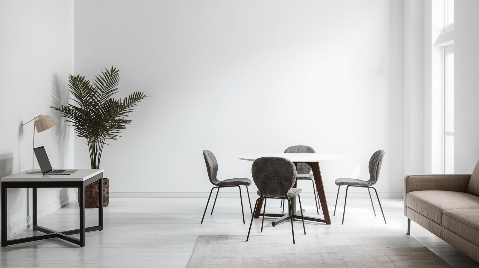 Jasne wnętrze z okrągłym stołem, czterema krzesłami i rośliną doniczkową. Na stole laptop i lampka. Minimalistyczny design, stonowana kolorystyka.