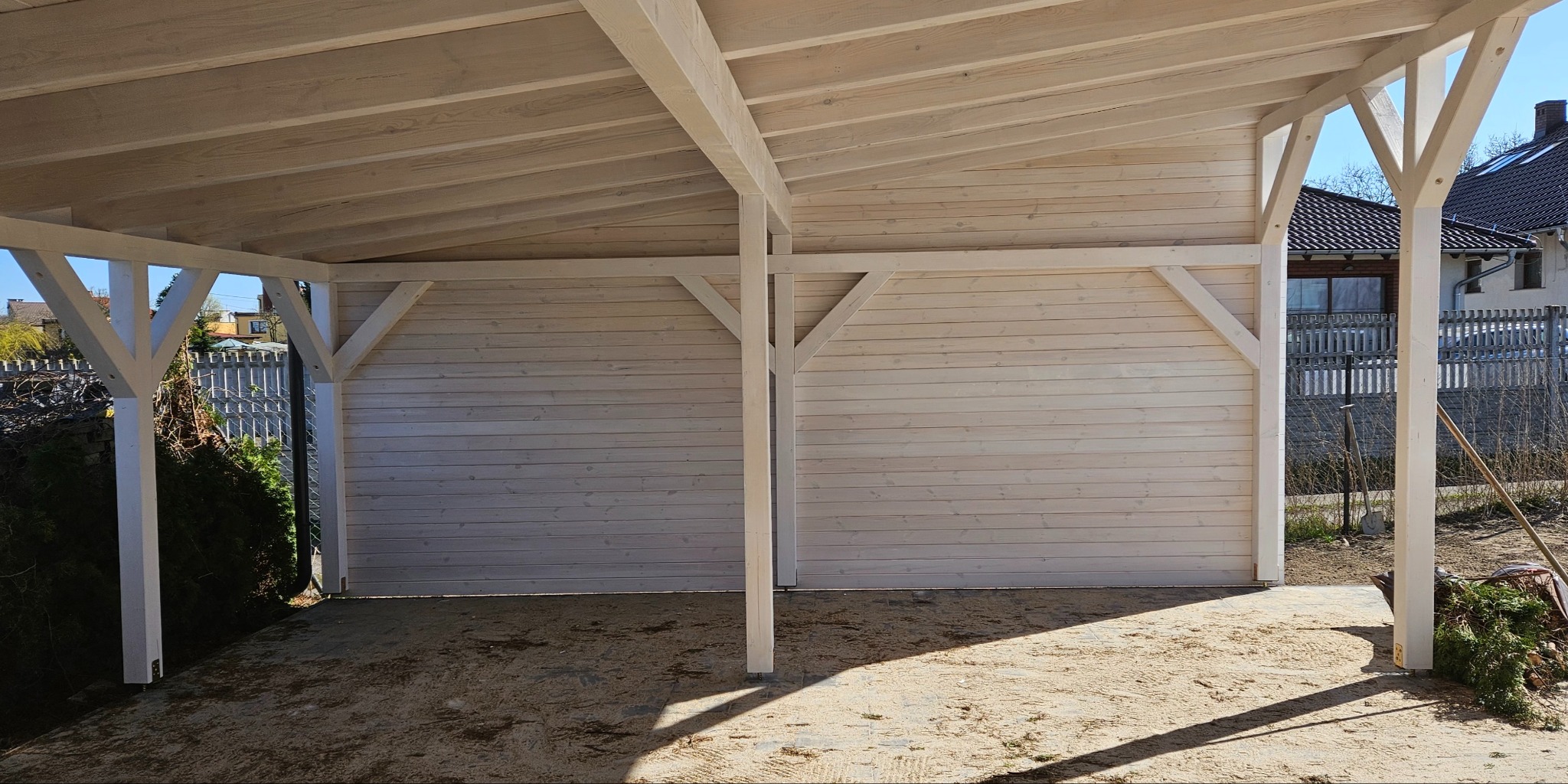 Drewniana altana z białym wykończeniem, widok z zewnątrz, konstrukcja z belek i desek, w tle zabudowa jednorodzinna.