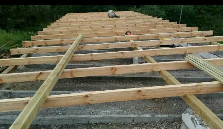 Konstrukcja drewniana dachu w trakcie budowy, widok z góry, z osobą pracującą w oddali i pilarką spalinową na konstrukcji.