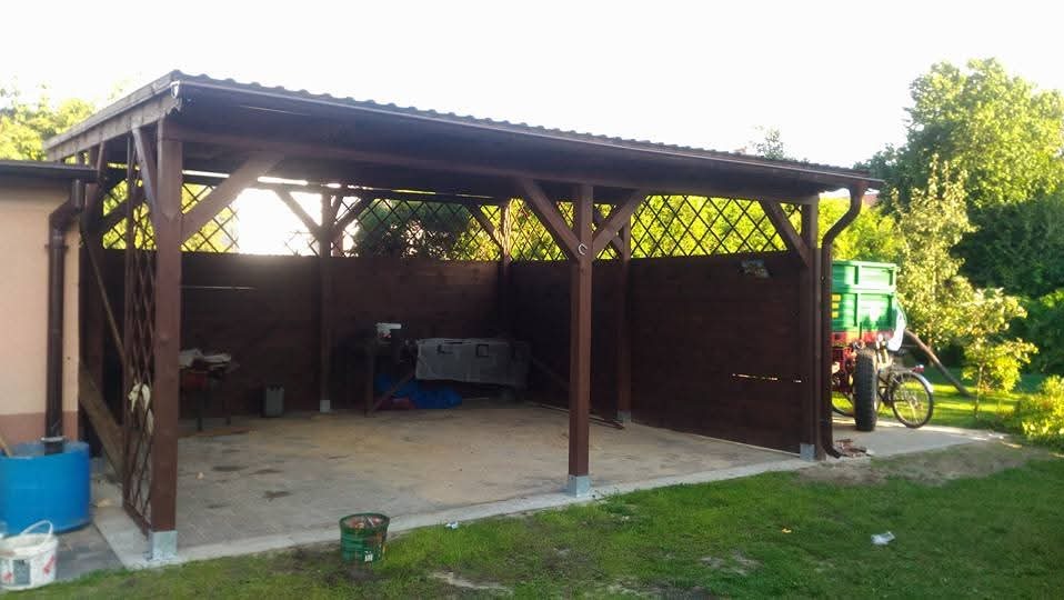 Zadaszona, drewniana konstrukcja z kratownicowymi ściankami, prawdopodobnie wiata lub garaż, z widocznym fragmentem dachu i rynny, na betonowej wylewce, z elementami wyposażenia wewnątrz...