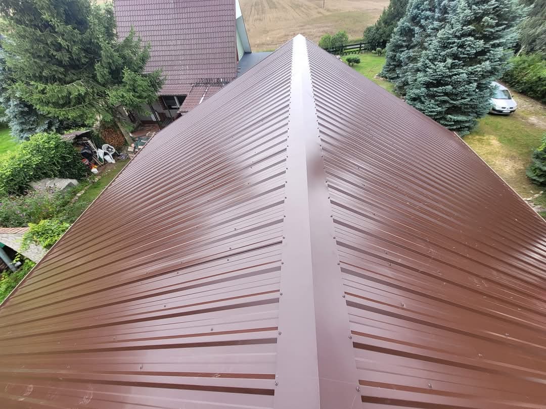 Nowe, brązowe pokrycie dachowe z blachy trapezowej, widok z góry na dom w otoczeniu zieleni.