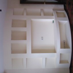 Veltrix - Ściana z wnękami i gładzią w odcieniach bieli, z widocznymi gniazdkami elektrycznymi i drewnianą podłogą parkietową w tle.