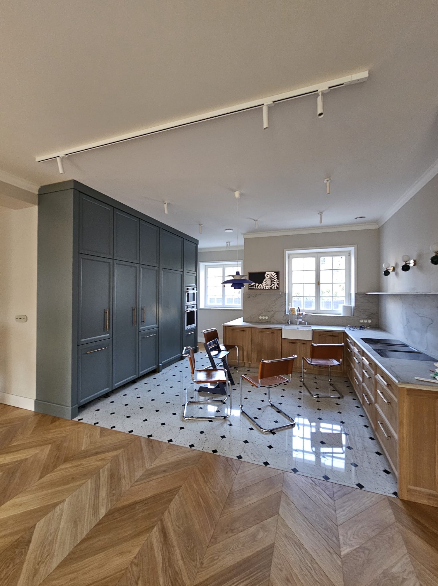 Nowoczesna kuchnia w Warszawie z szarymi szafkami, drewnianymi blatami i podłogą w jodełkę, oświetlona listwą LED.