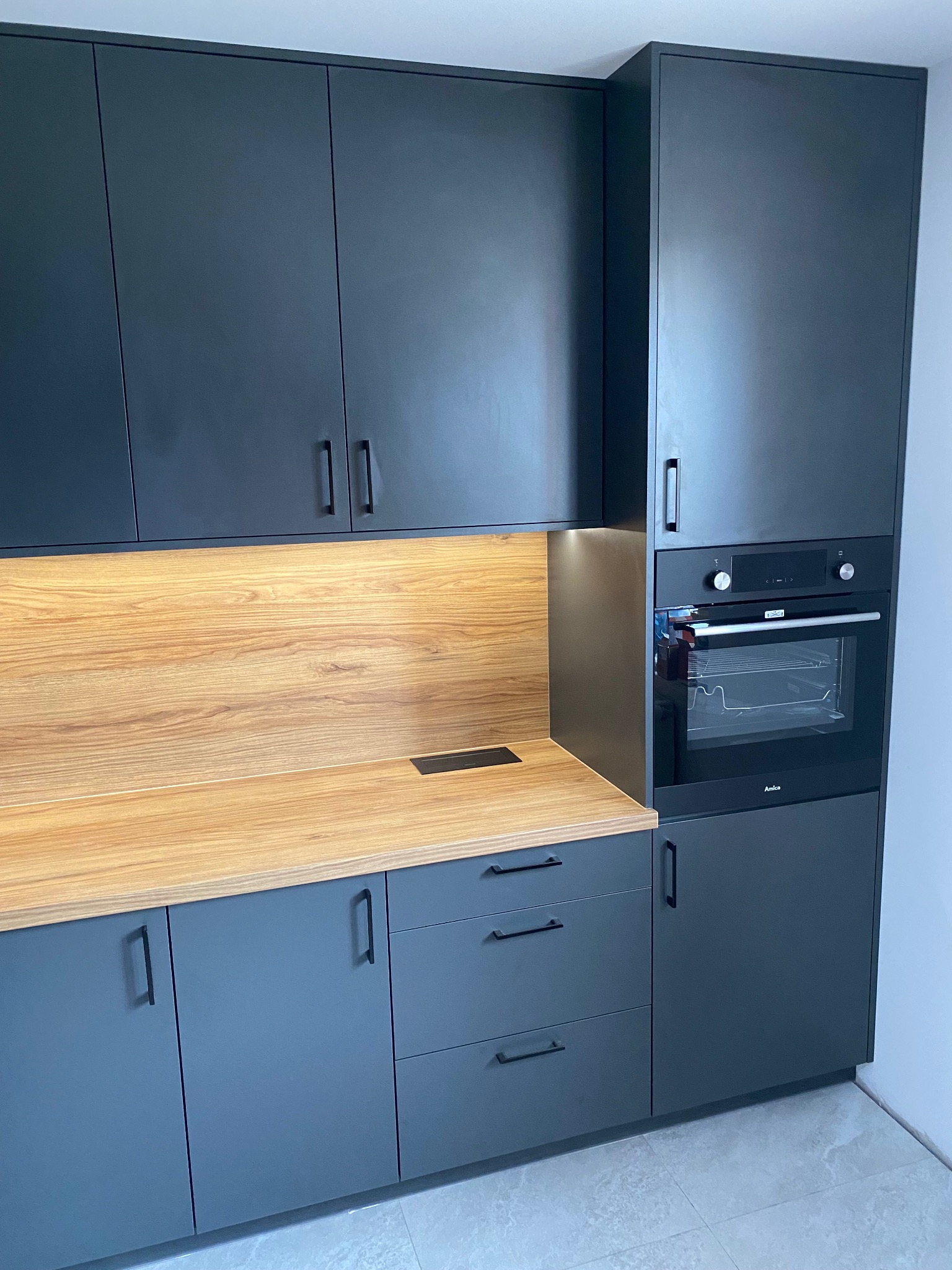 Nowoczesna kuchnia: grafitowe szafki z drewnianym blatem i wbudowanym piekarnikiem Amica, minimalistyczne uchwyty.