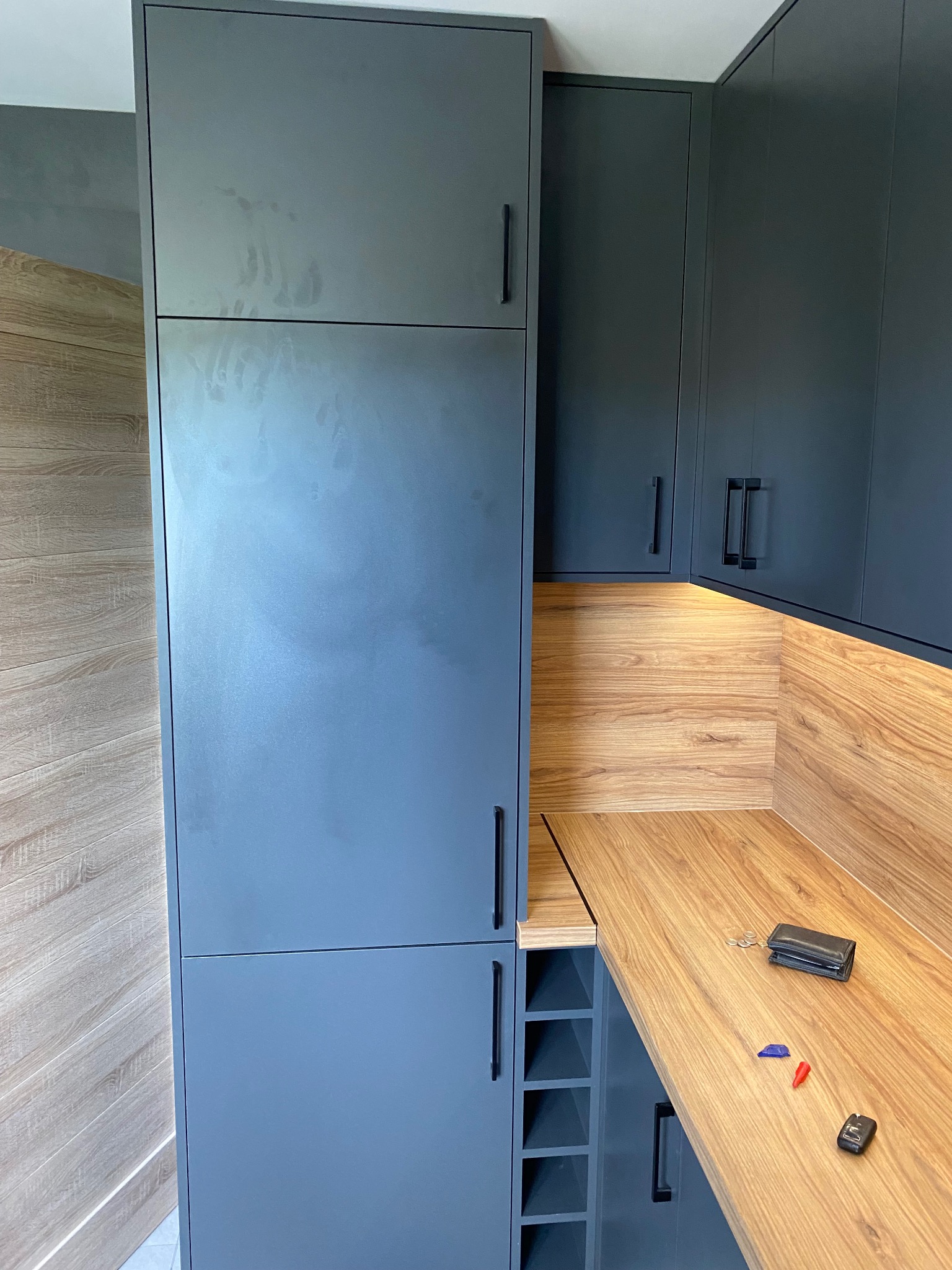 Szare matowe szafki kuchenne z drewnianym blatem, na którym leży portfel, klucze i monety. Widoczne ślady palców na górnej szafce.