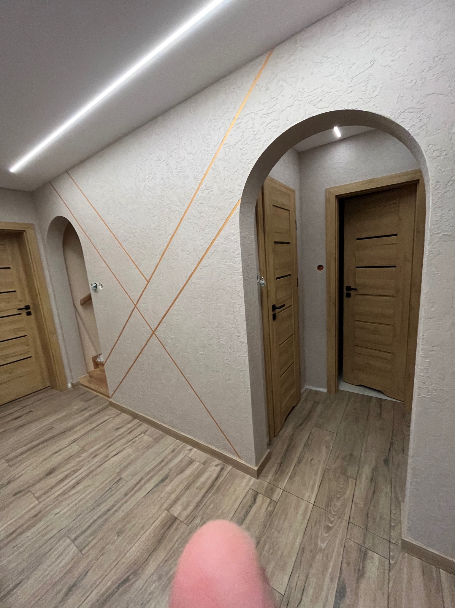 Aranżacja wnętrza: kremowe ściany z geometrycznym wzorem, drewniane drzwi w łukowatych przejściach i podłoga imitująca drewno. Nowoczesne oświetlenie sufitowe.