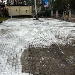 Zielony Tulipan - Częściowo oczyszczona kostka brukowa z resztkami piany i śladami po czyszczeniu, widoczny wąż ciśnieniowy, na tle budynek i drzewa.