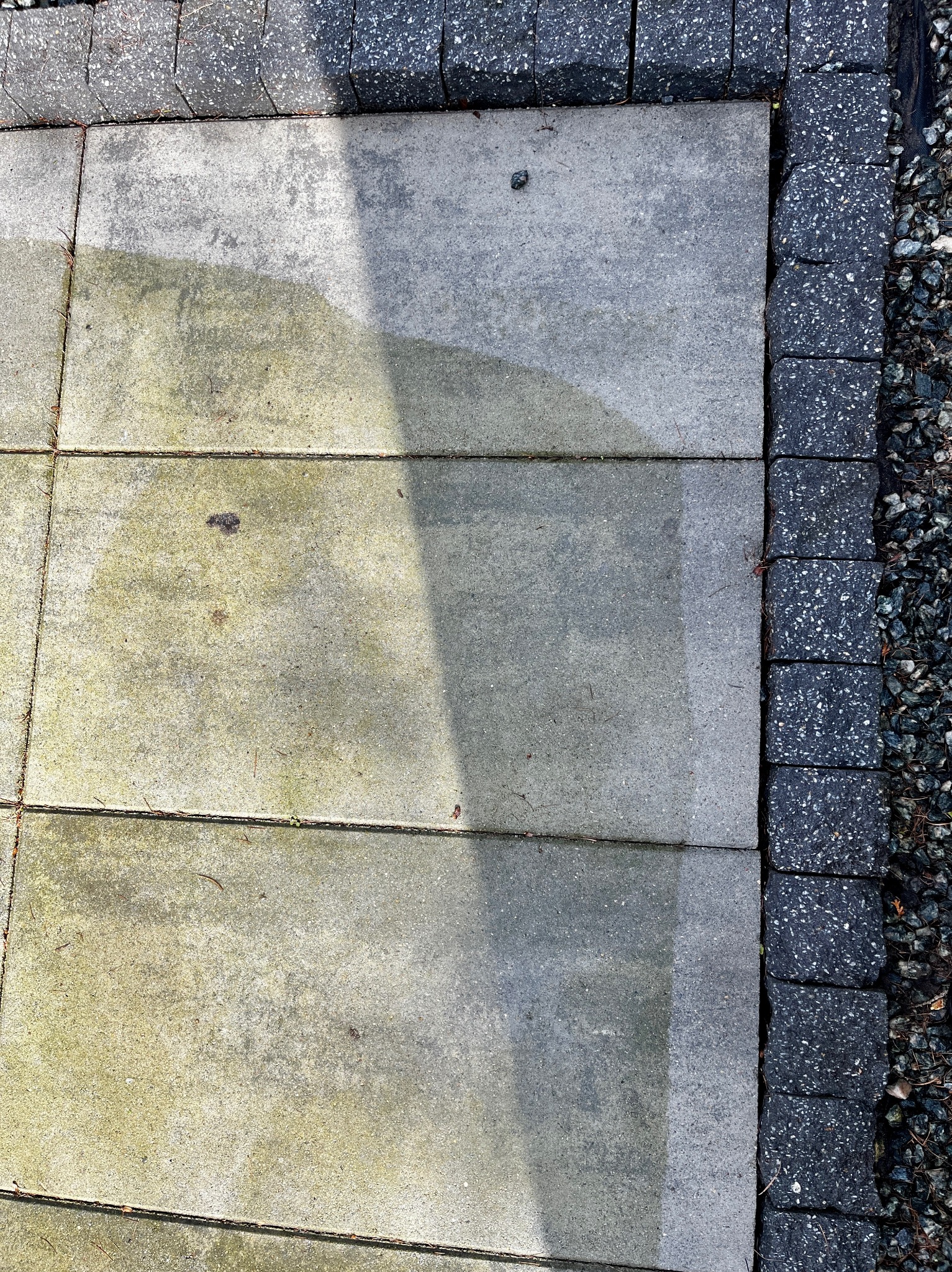 Fragment kostki brukowej, część umyta, część jeszcze zabrudzona mchem, z obrzeżem z ciemnej kostki i drobnymi kamykami.