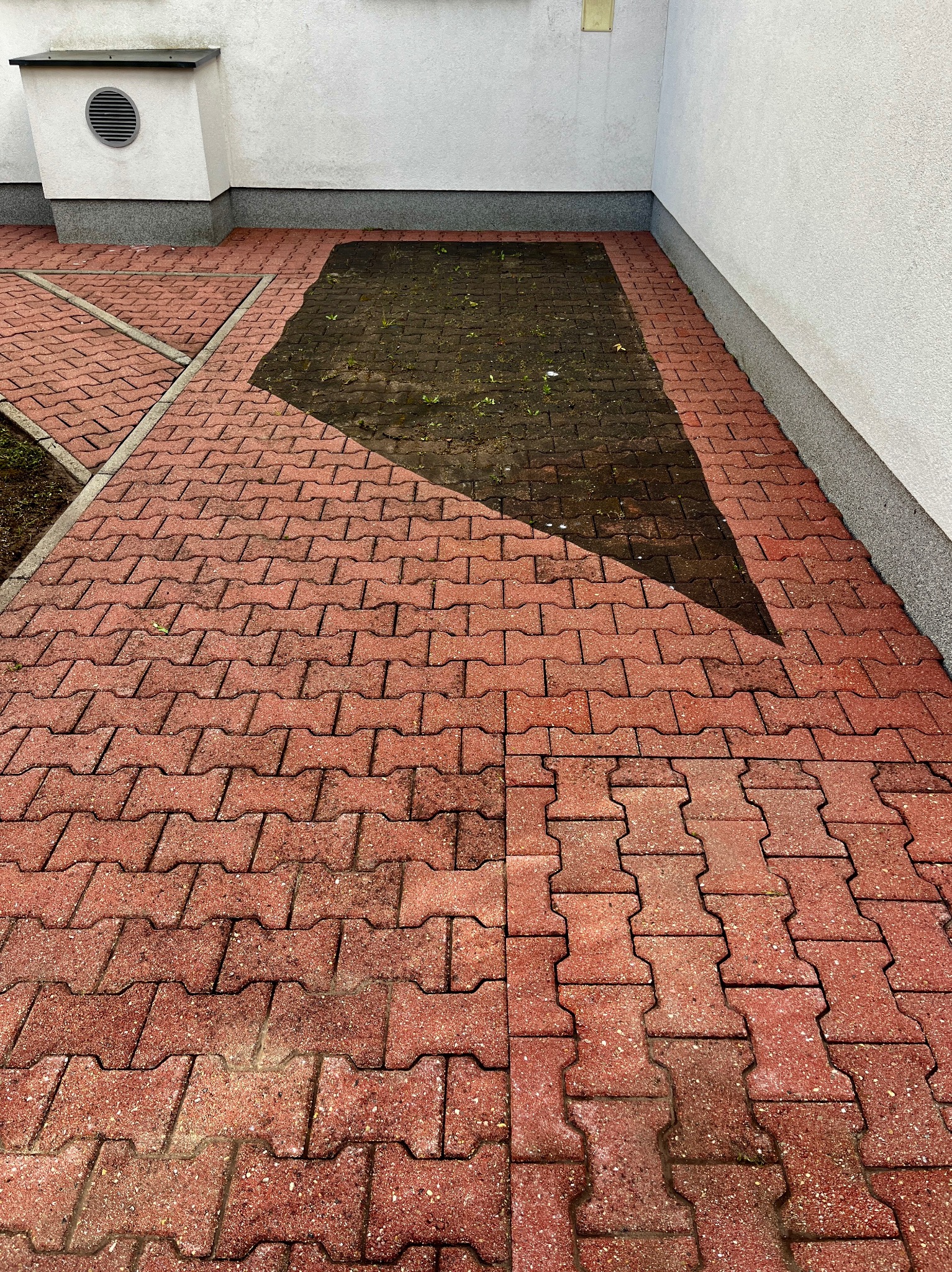 Częściowo wyczyszczona, czerwona kostka brukowa przed budynkiem. Widoczna różnica w kolorze i stopniu zabrudzenia, prezentująca efekt czyszczenia.