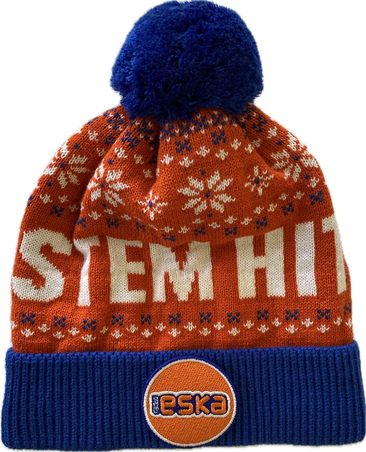 Pomarańczowa czapka zimowa z niebieskim pomponem i napisem 'STEM HIT', ozdobiona wzorem w śnieżynki i naszywką z logo 'ESKA'.